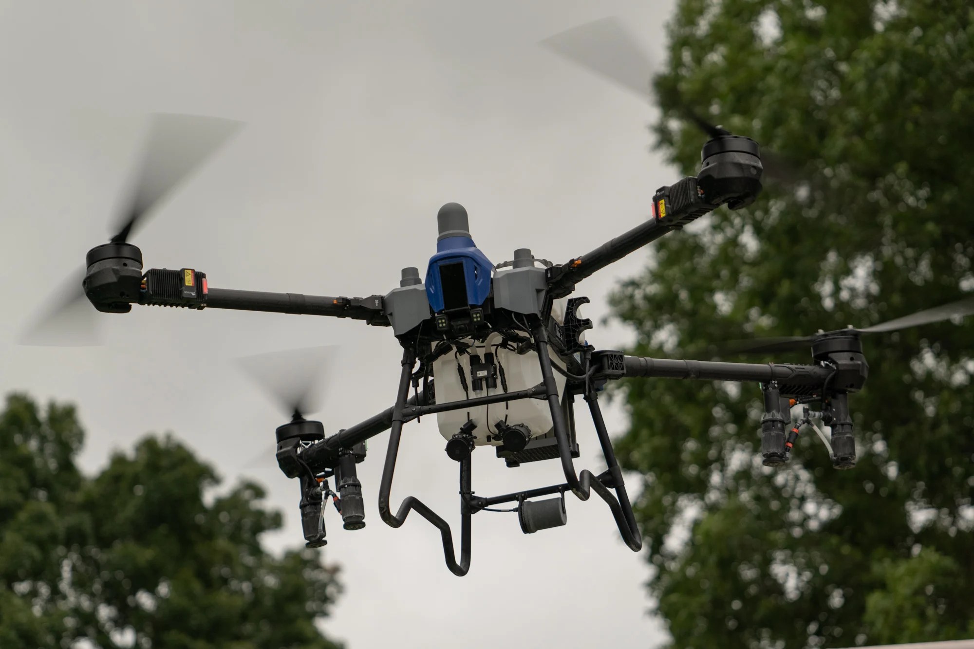 Close-up detail of the EAVision J150 spray drone in flight showing spray nozzles, camera array, and booms