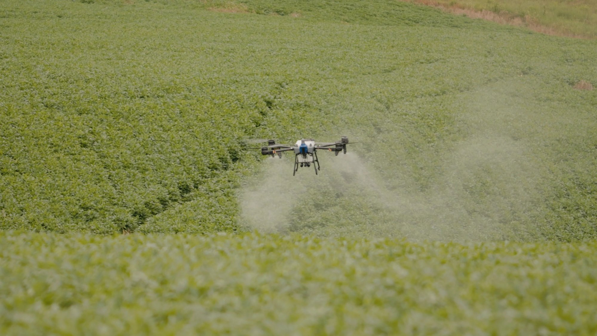 EAVision J150 spray drone applying product over a green soybean field